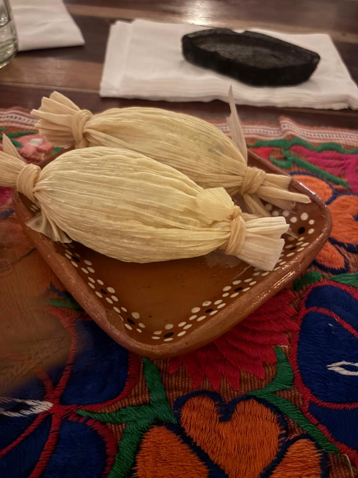 Traditional tamales wrapped in corn husks served on a decorative clay plate at Cetli