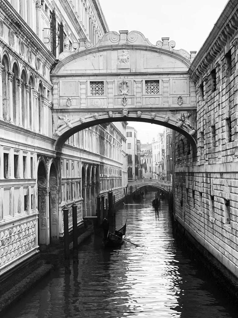 Black and white photo of the Bridge of Sighs spanning a narrow canal with a gondola below